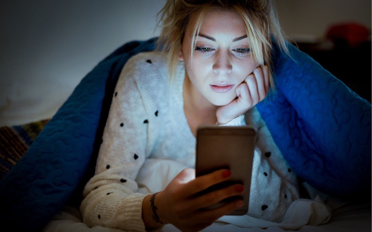 eine Frau liegt in ihrem Bett und schaut sich etwas auf ihrem Handy an