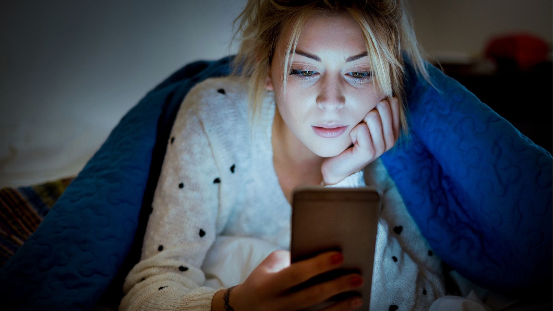 eine Frau liegt in ihrem Bett und schaut sich etwas auf ihrem Handy an