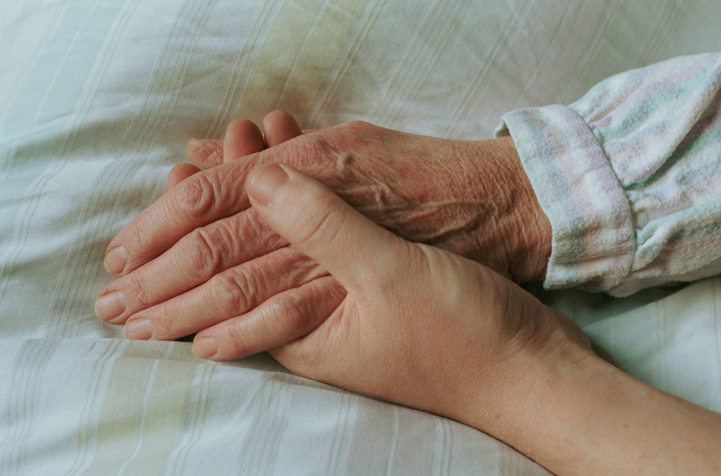 Einer alten Frau wird im Bett die Hand gehalten 