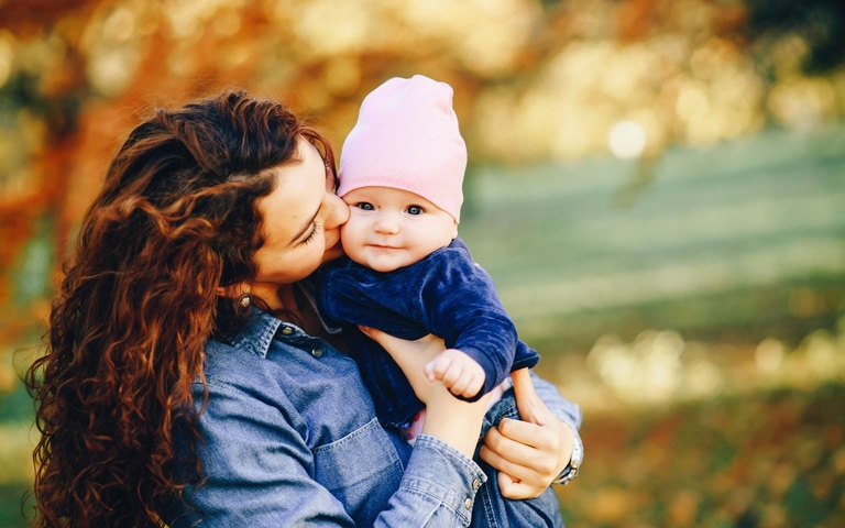 Eine junge Mutter herzt ihr Baby, welches selig in die Kamera lächelt.