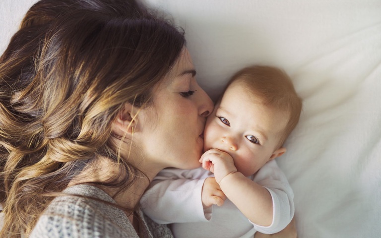 eine junge Mutter gibt ihrem Baby einen Kuss auf die Wange