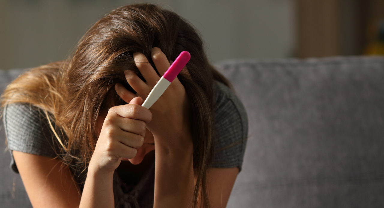 eine verzweifelte junge Frau mit Schwangerschaftstest - Ausnahmezustand