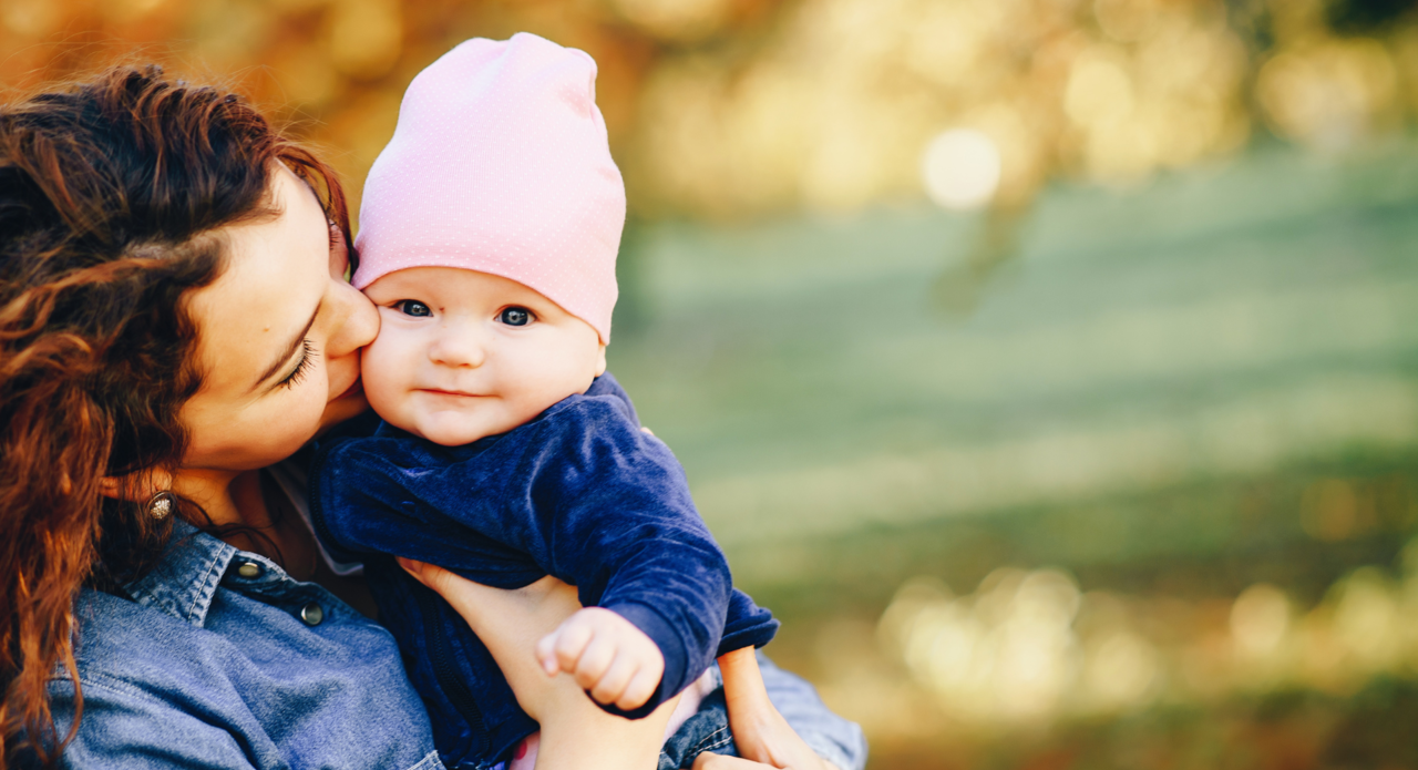 Eine junge Mutter herzt ihr Baby, welches selig in die Kamera lächelt.