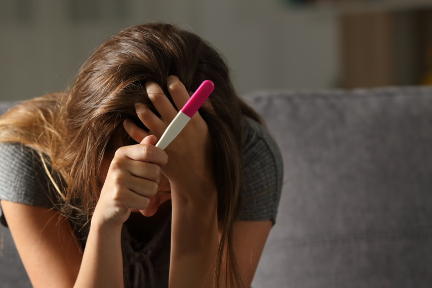 eine verzweifelte junge Frau mit Schwangerschaftstest - Ausnahmezustand