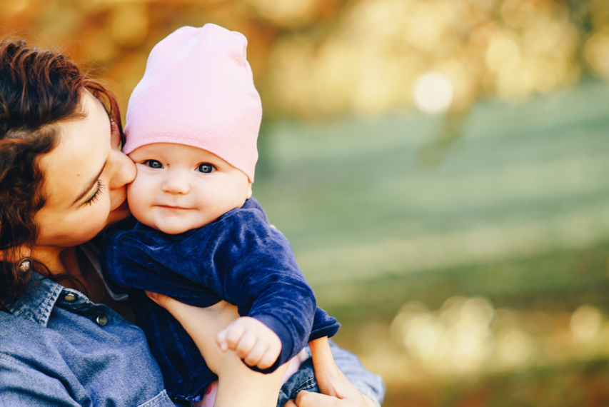 Eine junge Mutter herzt ihr Baby, welches selig in die Kamera lächelt.